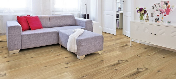 Im Wohnzimmer ist Parkett in Langdielen-Optik verlegt. Dazu passt ein Ecksofa mit bunten Kissen.