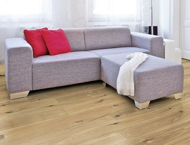 Im Wohnzimmer ist Parkett in Langdielen-Optik verlegt. Dazu passt ein Ecksofa mit bunten Kissen.