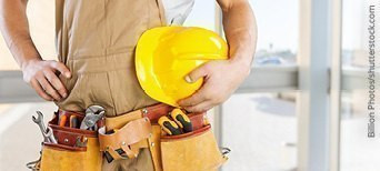 Handwerker mit gelbem Schutzhelm und Werkzeuggürtel, bereit für den Einsatz auf der Baustelle.
