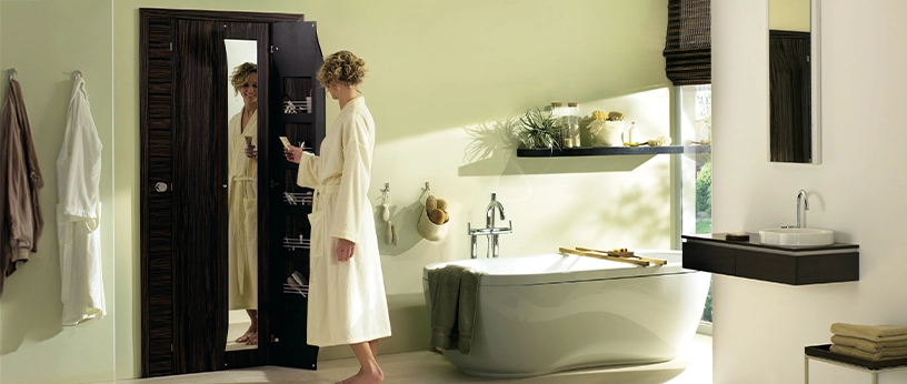 Badezimmertür mit Spiegel in dunklem Holzdekor, Frau im Bademantel, freistehende Badewanne.