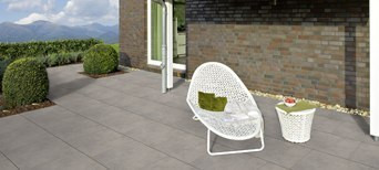 Moderne Terrasse mit großen grauen Fliesen, weißem Loungesessel, Beistelltisch und Blick auf die Berge.