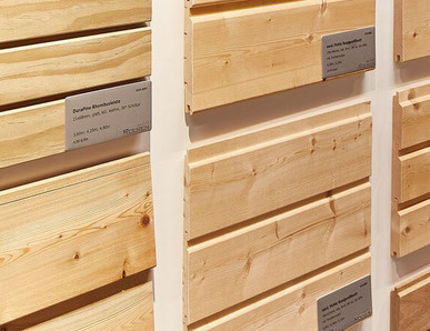 Ausstellung von verschiedenen gehobelten Holzprofilen mit Beschriftung, geeignet für Fassaden- und Innenverkleidung.