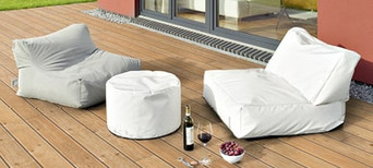 Holzterrasse mit bequemen Sitzsäcken, weißem Pouf und stilvoll arrangiertem Wein und Snacks.